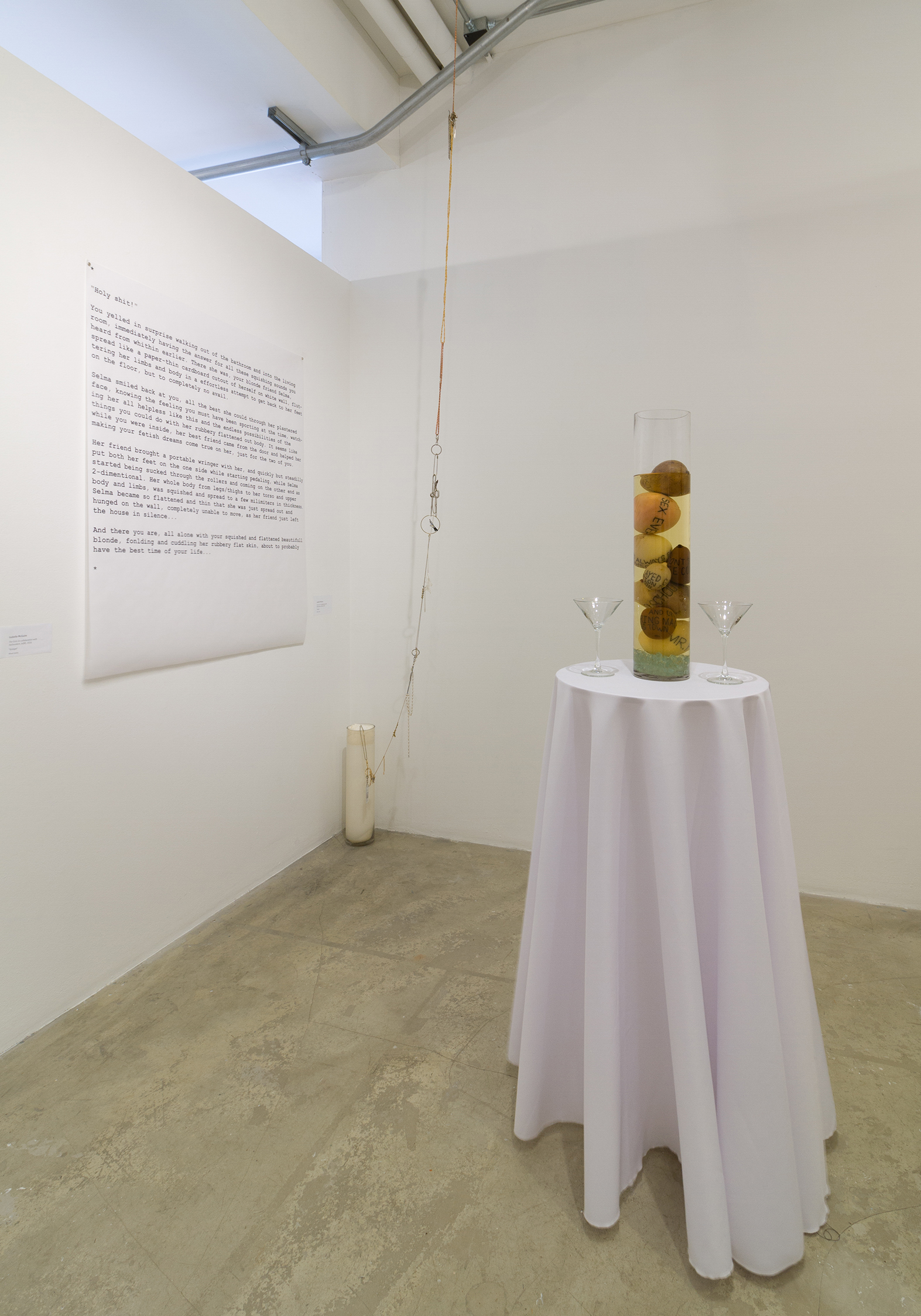 Installation view of one round table with fruit colums on them and a text print in a white wall gallery